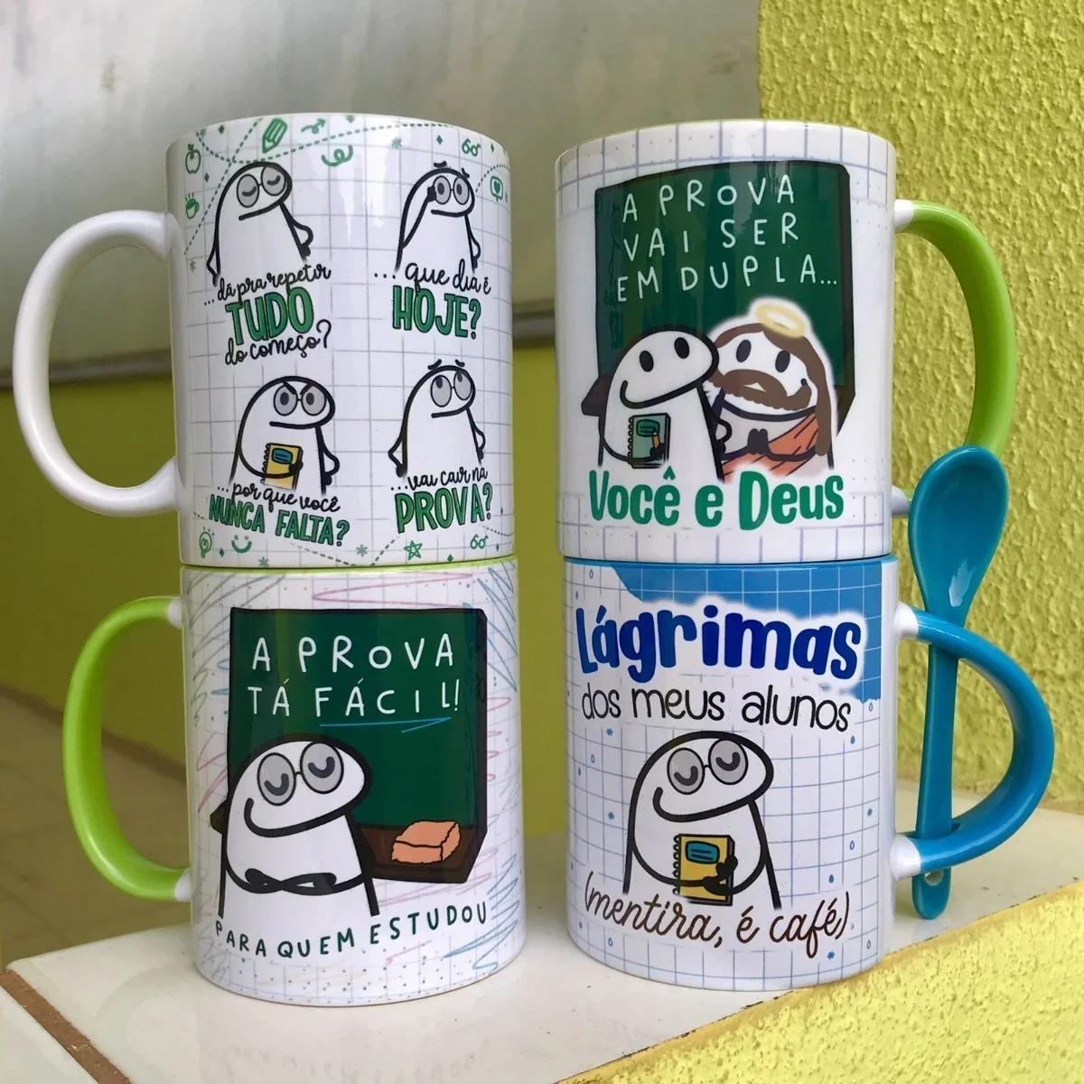 Quatro canecas brancas estampadas com desenhos humorísticos e frases em português.