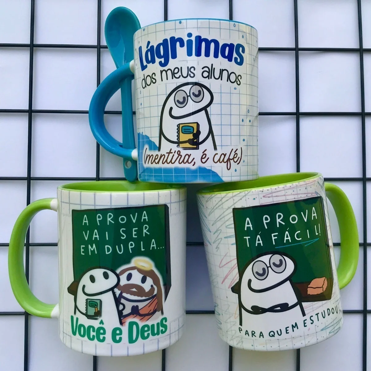 Tres canecas estampadas com frases engraçadas e desenhos estilo cartoon sobre professores e provas.