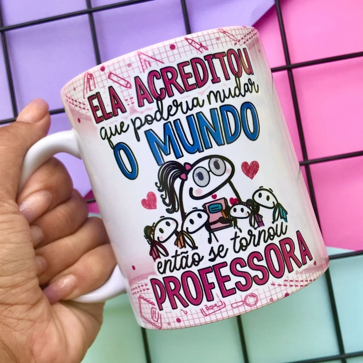 Mão segurando caneca branca com estampa colorida e frases sobre professores