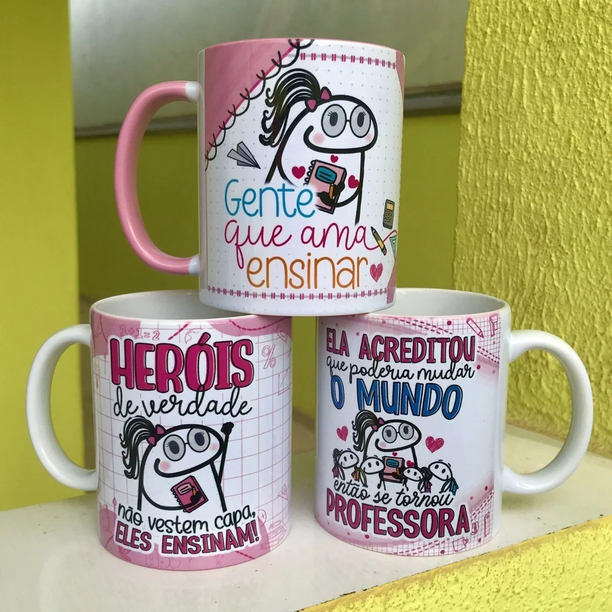 Tres canecas brancas com estampas coloridas sobre o tema de professores.