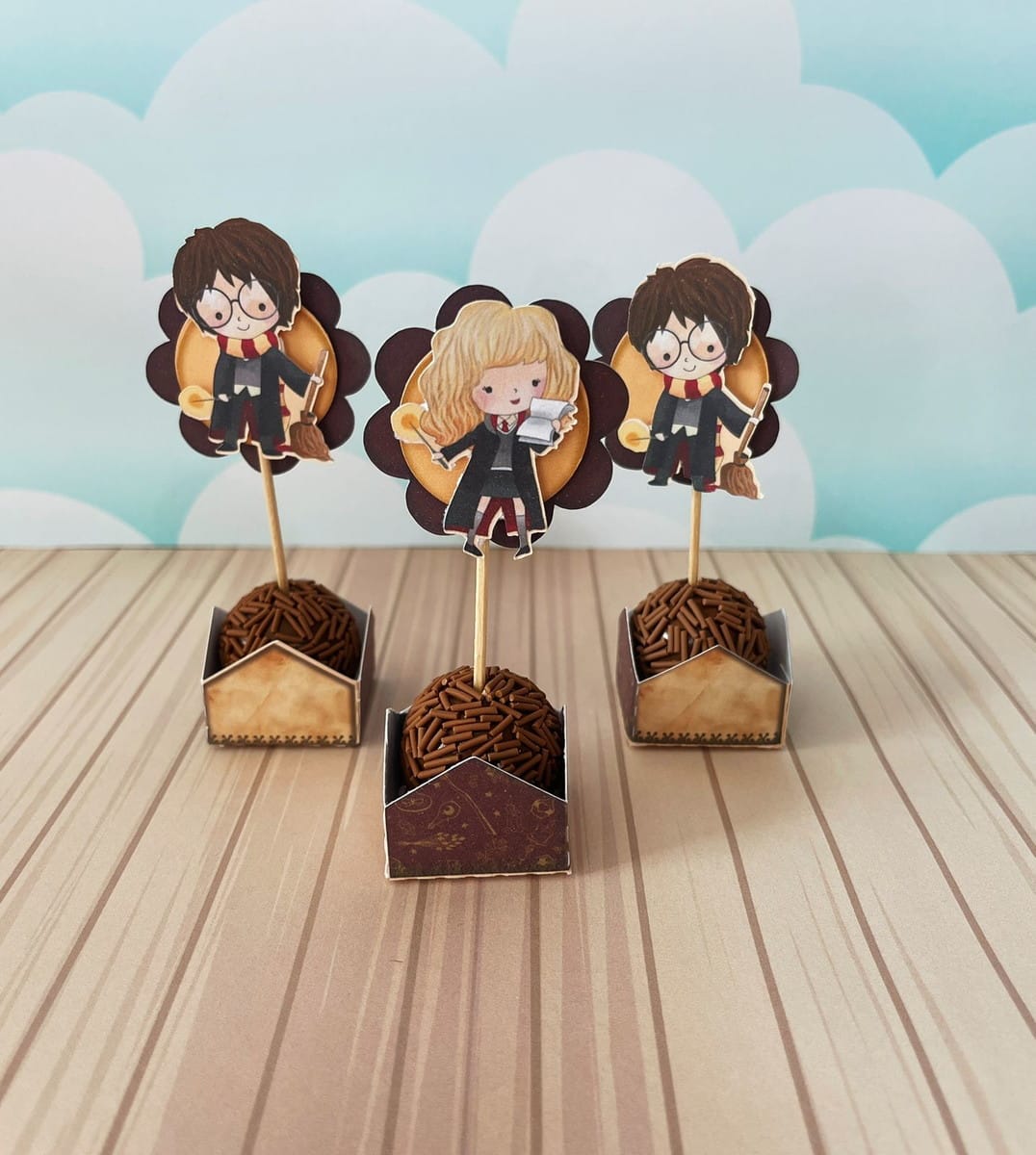 Arquivo de Corte Harry Potter para Festa em Studio e PDF 3 Três toppers de doces com personagens de fantasia, dois meninos e uma menina, em fundo de nuvens.