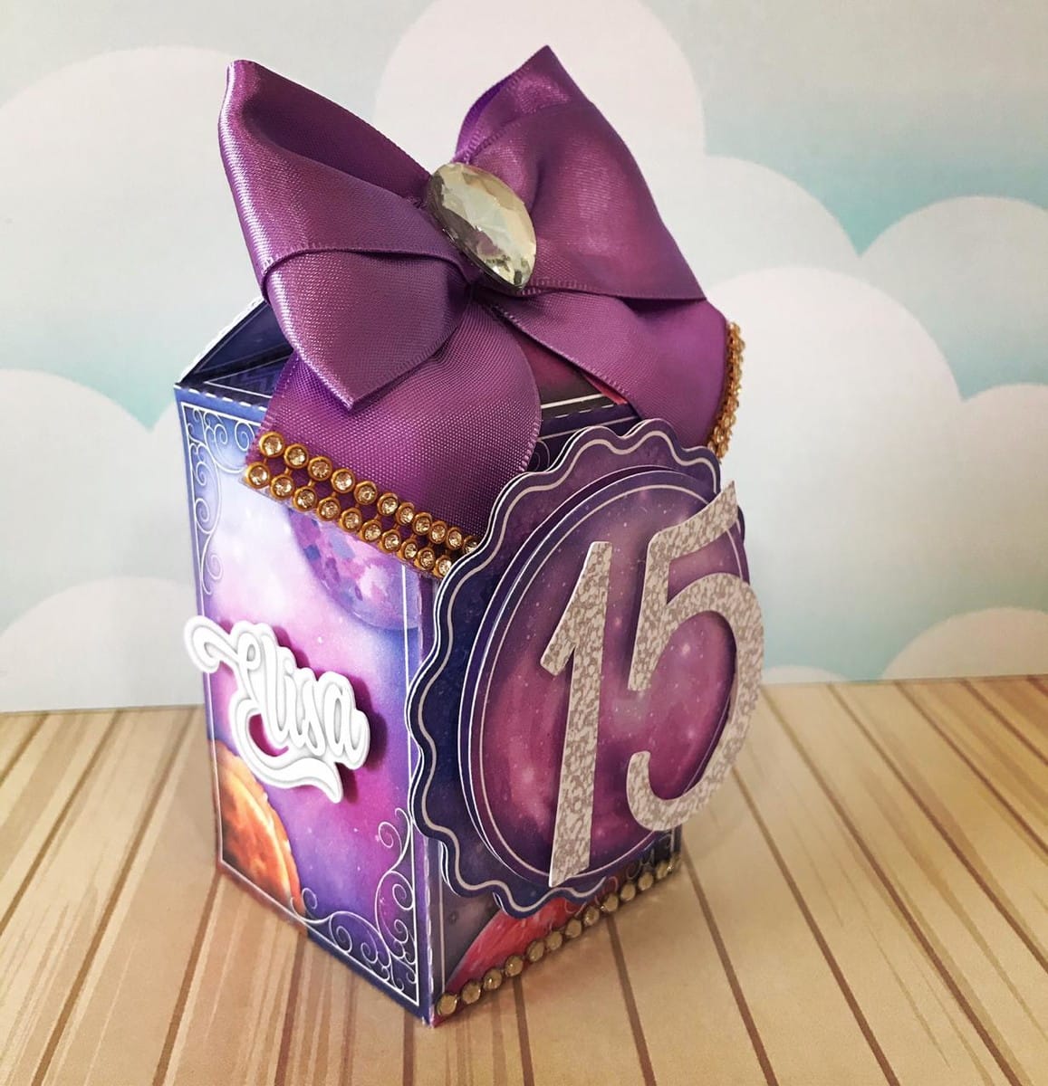 Arquivo de Corte Galáxia para Festa de 15 Anos 5 Caixa decorada temática espacial com laço roxo, número 15 e detalhes brilhantes.