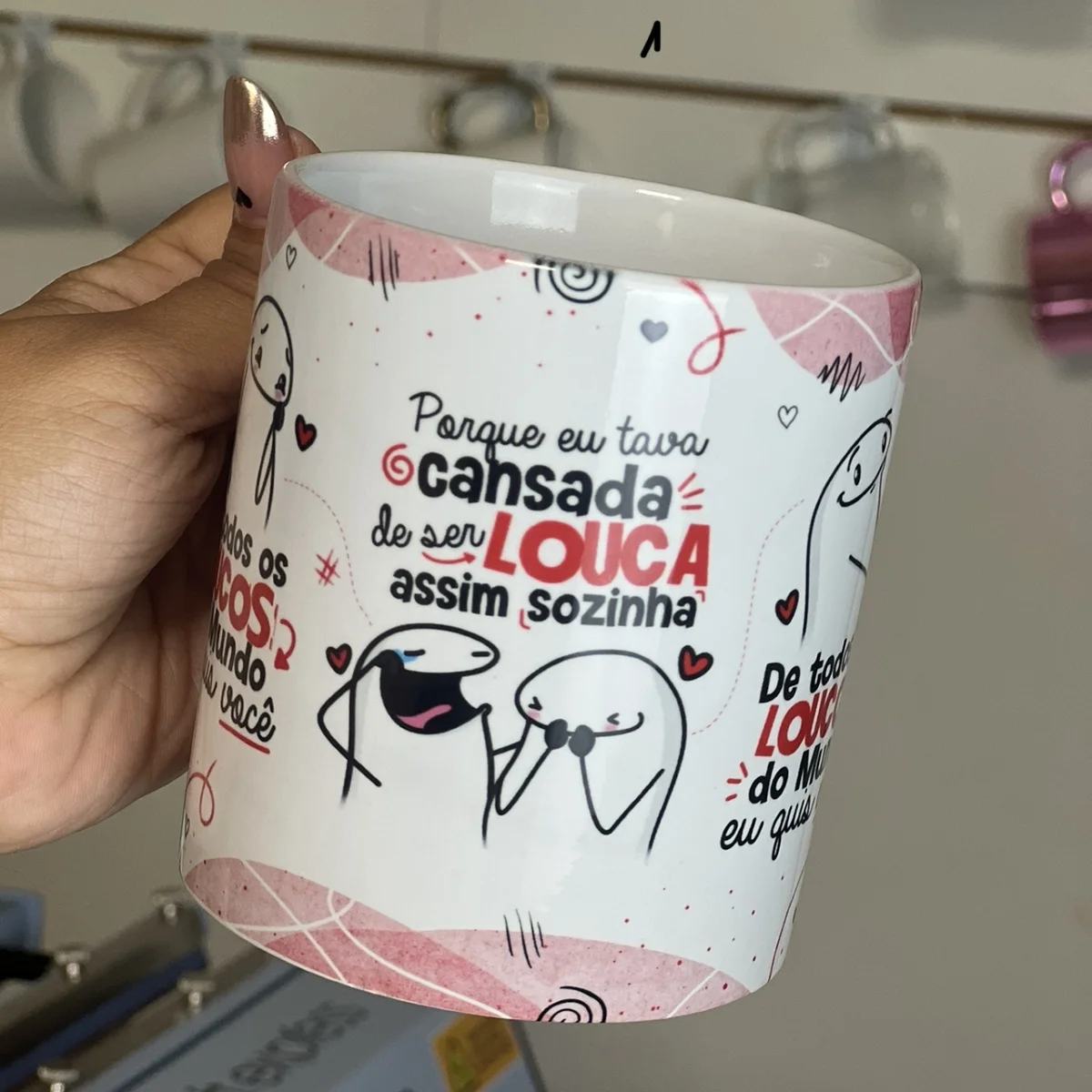 Mão segura caneca branca estampada com desenhos e textos em português.