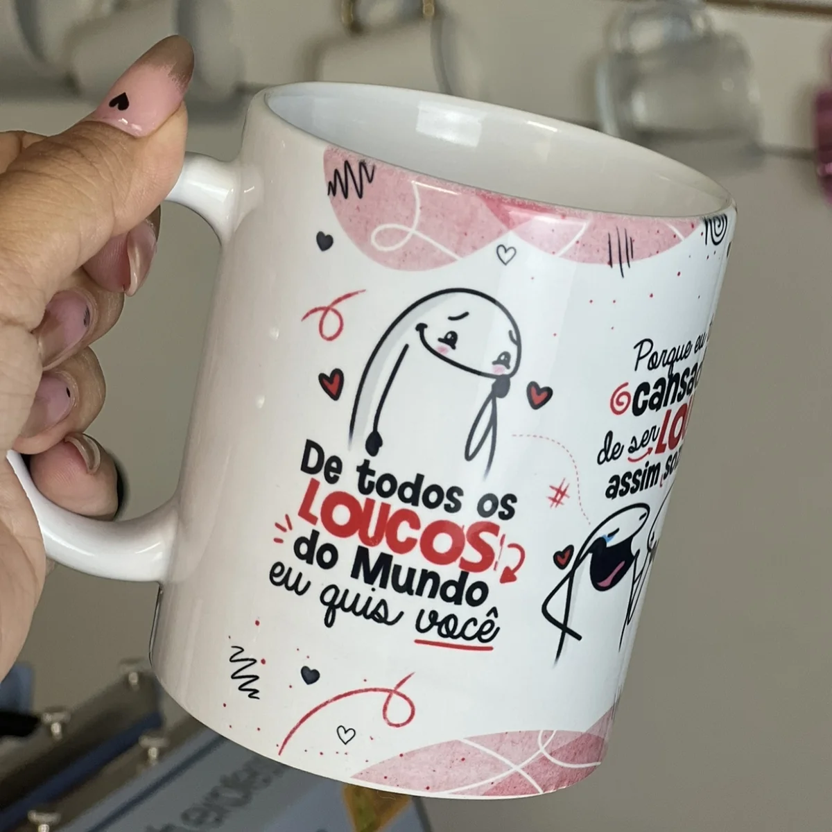 Mão segurando caneca branca estampada com desenho romântico e frase em português.
