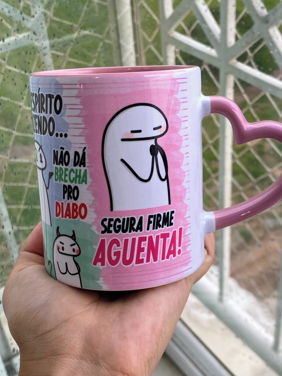 Arte Caneca Flork Png A Alma Tá Doida para Sublimação 2 Mão segurando caneca rosa com desenho de personagem e frases em português.