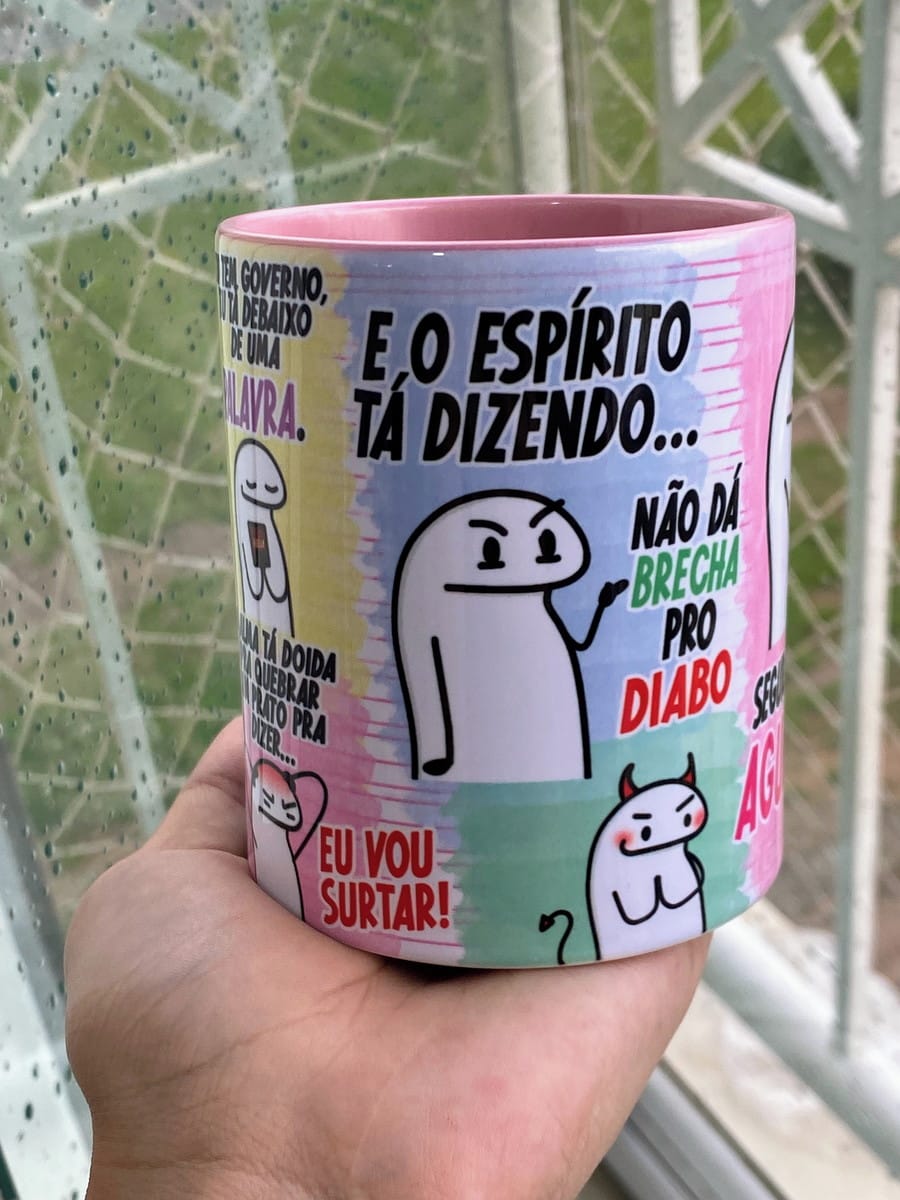 Arte Caneca Flork Png A Alma Tá Doida para Sublimação 1 Mão segurando caneca de cerâmica rosa com desenhos de personagens e frases cômicas.