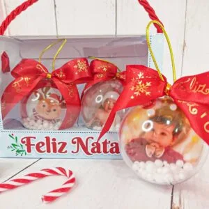 Três bolas de natal transparentes com fotos personalizadas e laços vermelhos.
