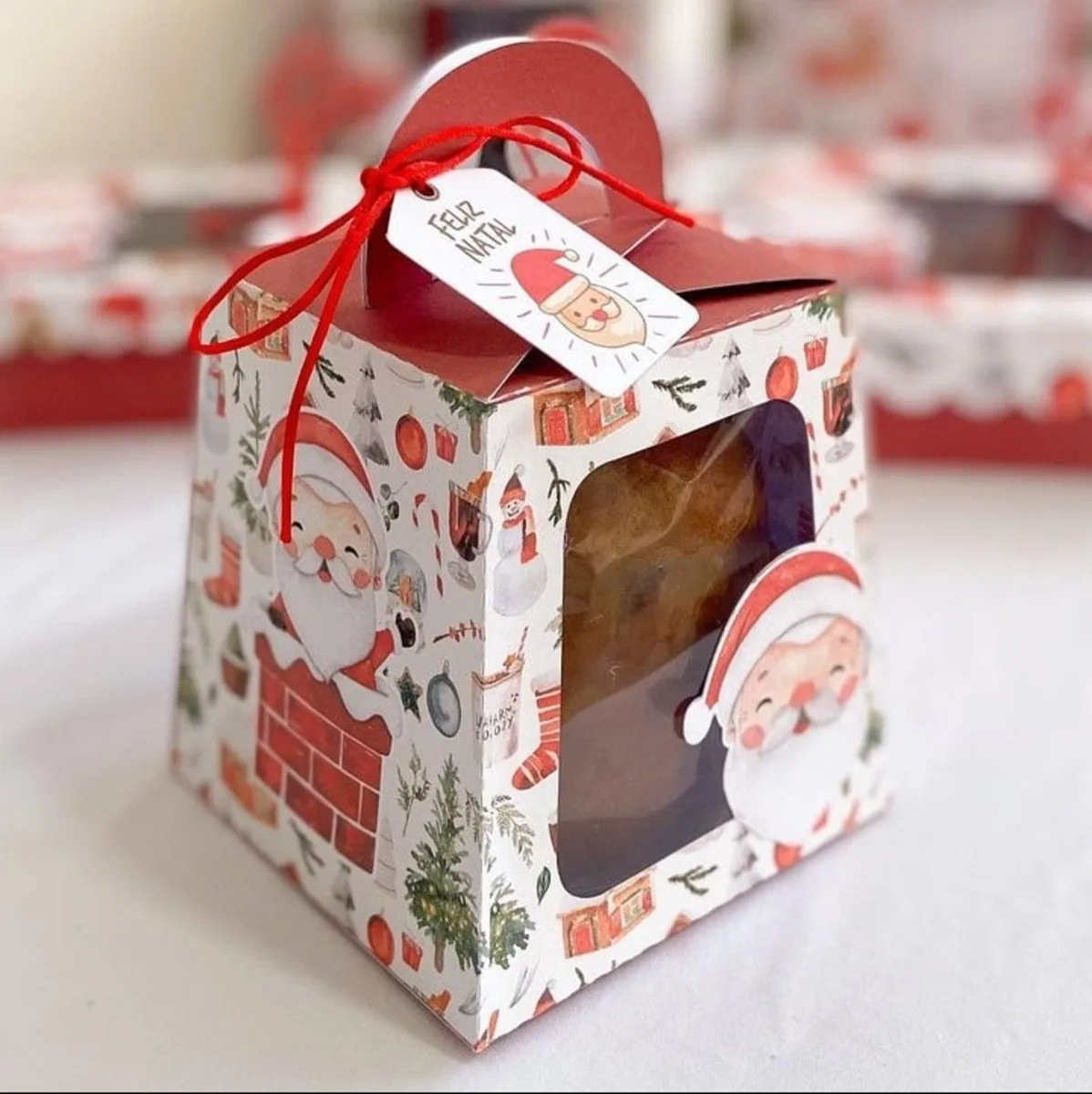 Caixa de presente com tema de Natal, ilustrações de Papai Noel e laço vermelho.
