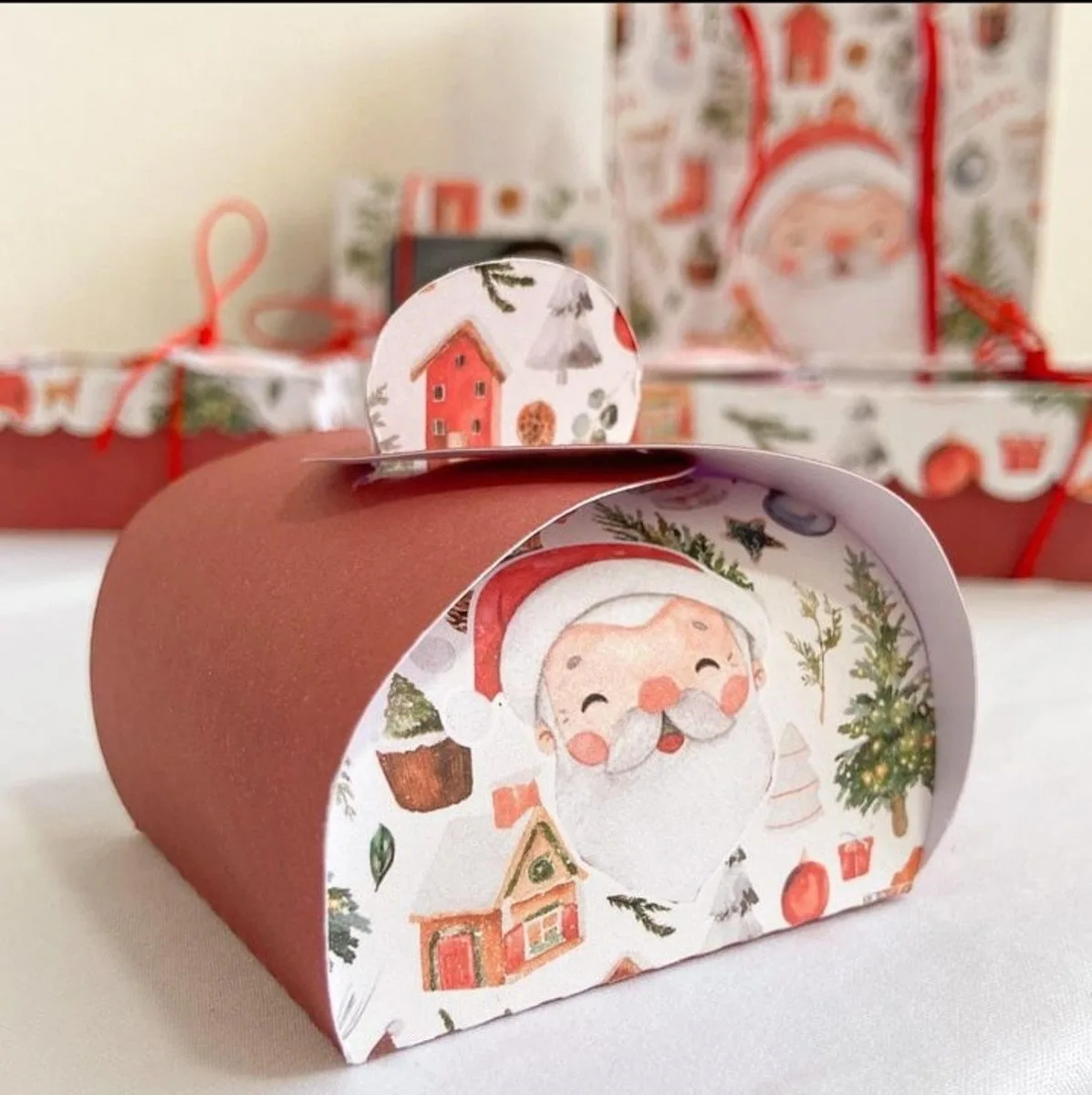 Caixa de papel com estampa natalina de Papai Noel e casas.