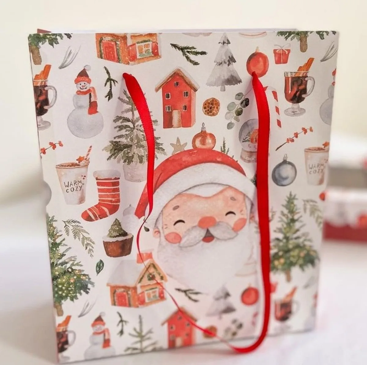 Saco de presente decorado com ilustrações natalinas coloridas e alças vermelhas.