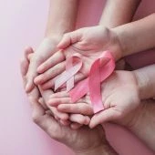 Mãos unidas segurando duas fitas rosa contra fundo rosa claro
