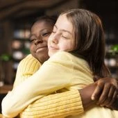 Duas meninas jovens se abraçam carinhosamente em um ambiente interno aconchegante e escuro.