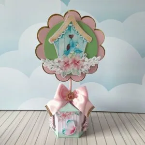 Decoração de mesa em camadas com casinha de pássaro e laço de fita rosa.