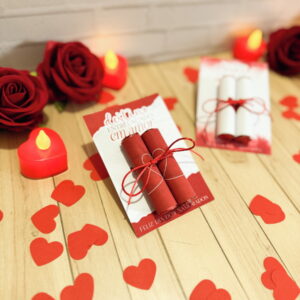 Arte digital de cartão vermelho com rolos e laço, cercado por corações e rosas.