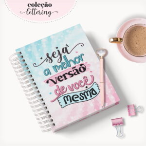 Caderno espiral colorido com frase escrita na capa e xícara de café.
