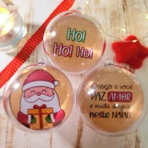 Três bolas de Natal transparentes com desenhos e frases sobre fundo branco decorado.