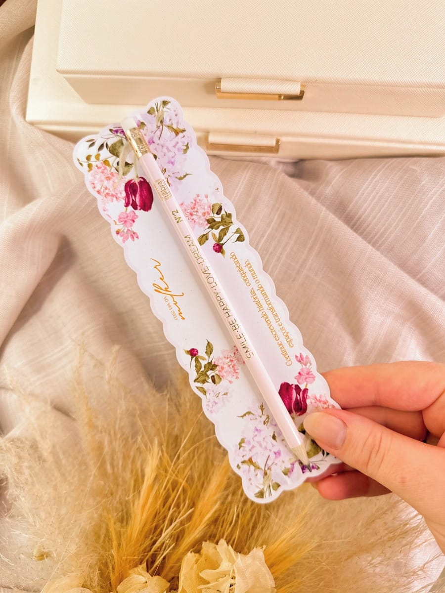 Kit Digital Dia da Mulher Cristão para Personalizados 5 Mão segura um marcador de página decorado com flores e um lápis rosa.