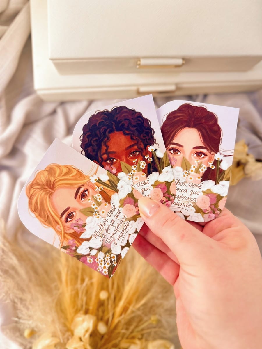 Kit Digital Dia da Mulher Cristão para Personalizados 1 Mão segurando três cartões ilustrados com rostos de mulheres e flores.