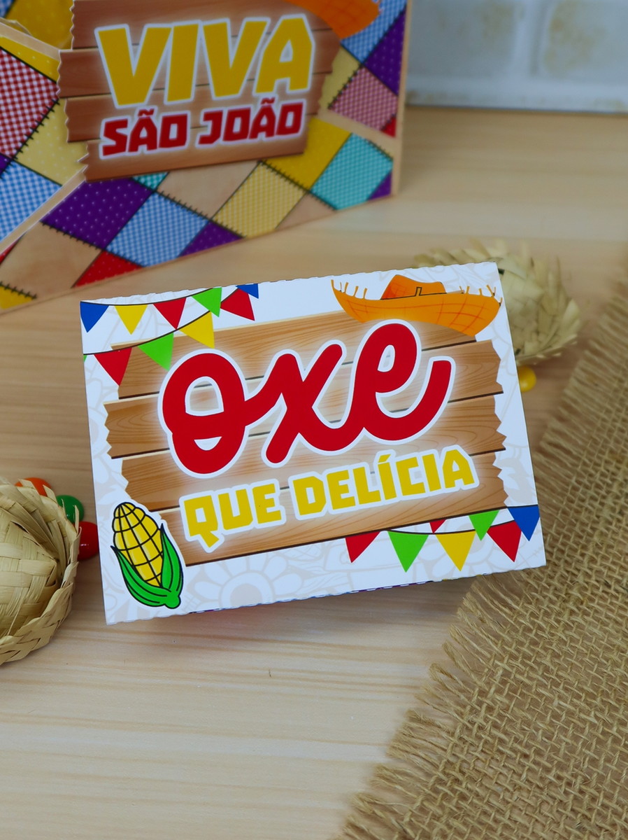 Kit digital Festa Junina Studio para lembrancinhas 5 Caixa de papel personalizada com tema festivo e ilustrações coloridas sobre mesa de madeira.