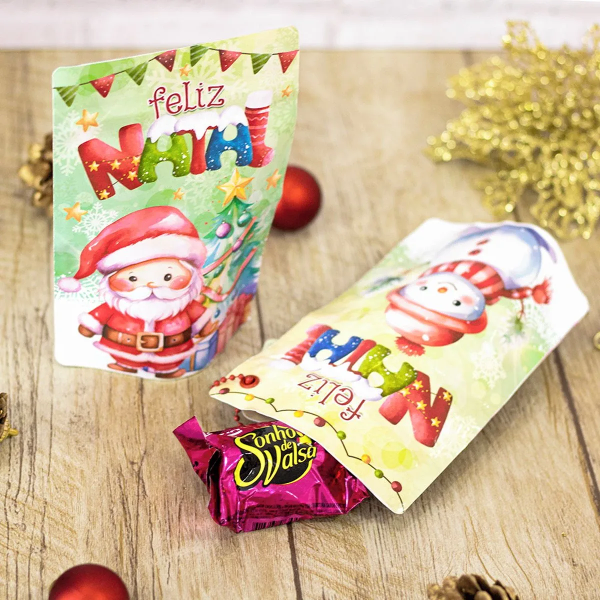 Dois saquinhos de Natal personalizados sobre uma mesa de madeira com doce.
