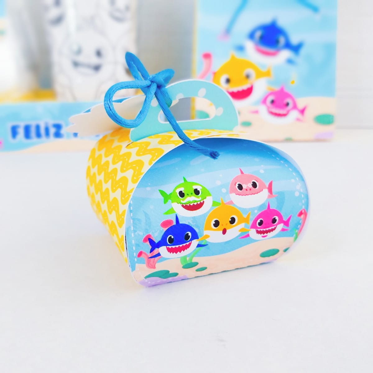 Kit digital Páscoa Baby Shark com caixas e sacolinhas 4 Arte digital de tubarões coloridos para caixa de festa, com laço azul e fundo festivo.