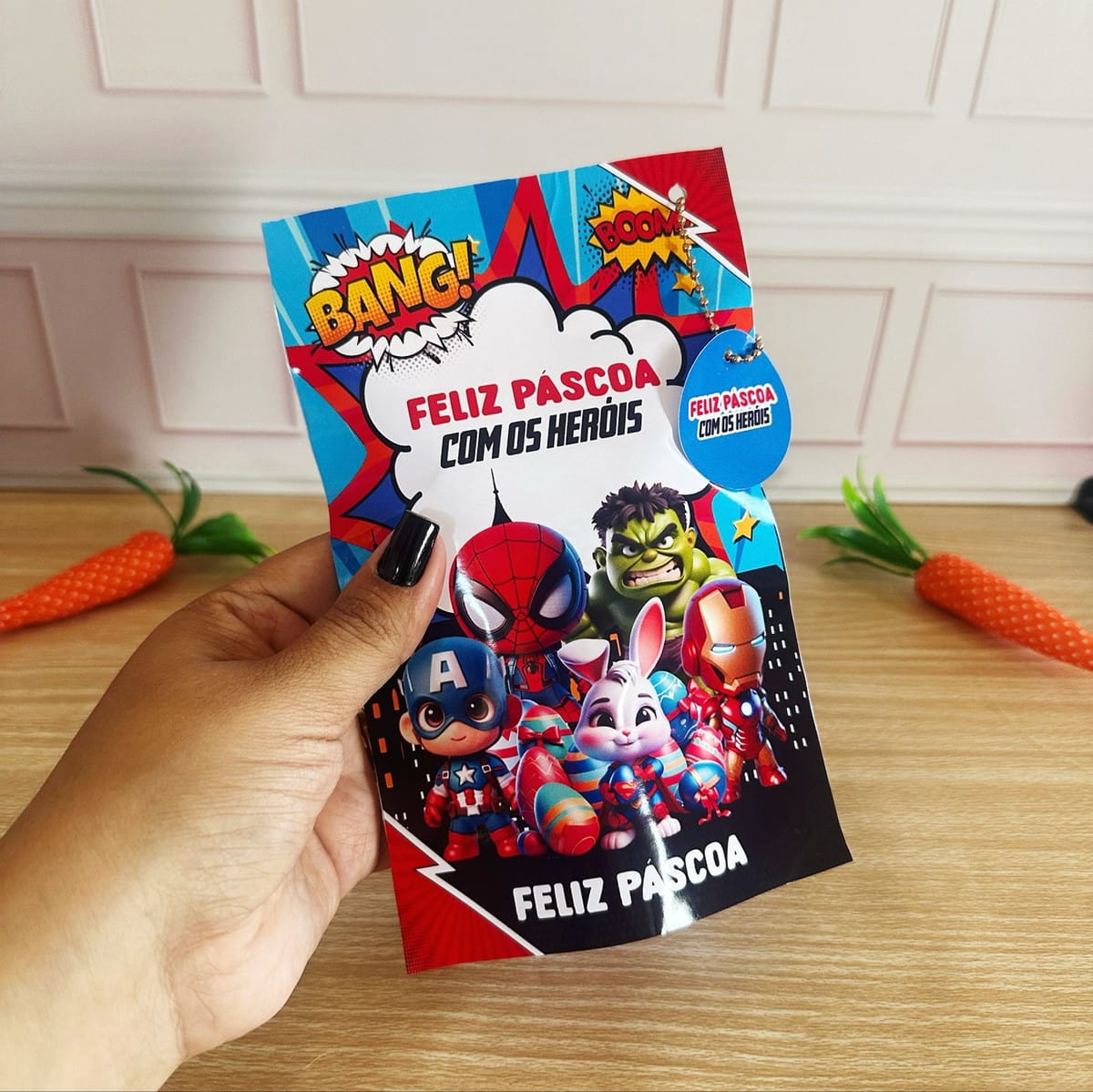 Kit Digital Páscoa Super Heróis para Corte e Impressão 2 Design de Páscoa colorido com personagens de heróis e coelho, segurado por uma mão.