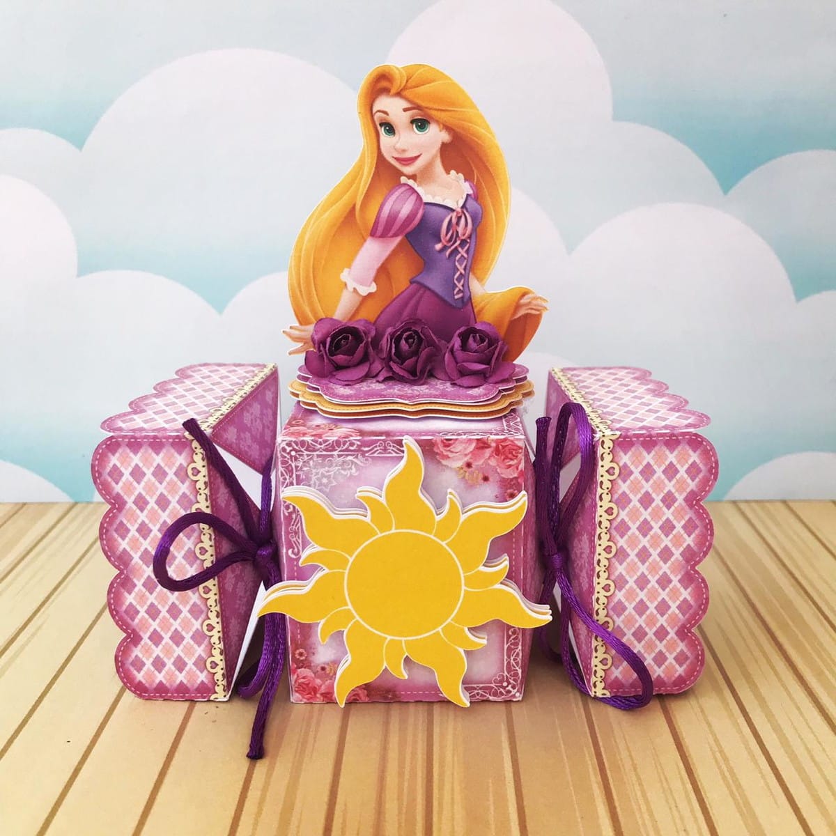 Kit Digital Rapunzel Festa Infantil com Caixas e Convites 2 Arte digital de caixa decorativa com personagem feminina de cabelos loiros e sol amarelo.