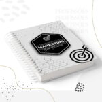 Caderno espiral branco com capa geométrica, adesivo hexagonal "MARKETING" e ícone de alvo.