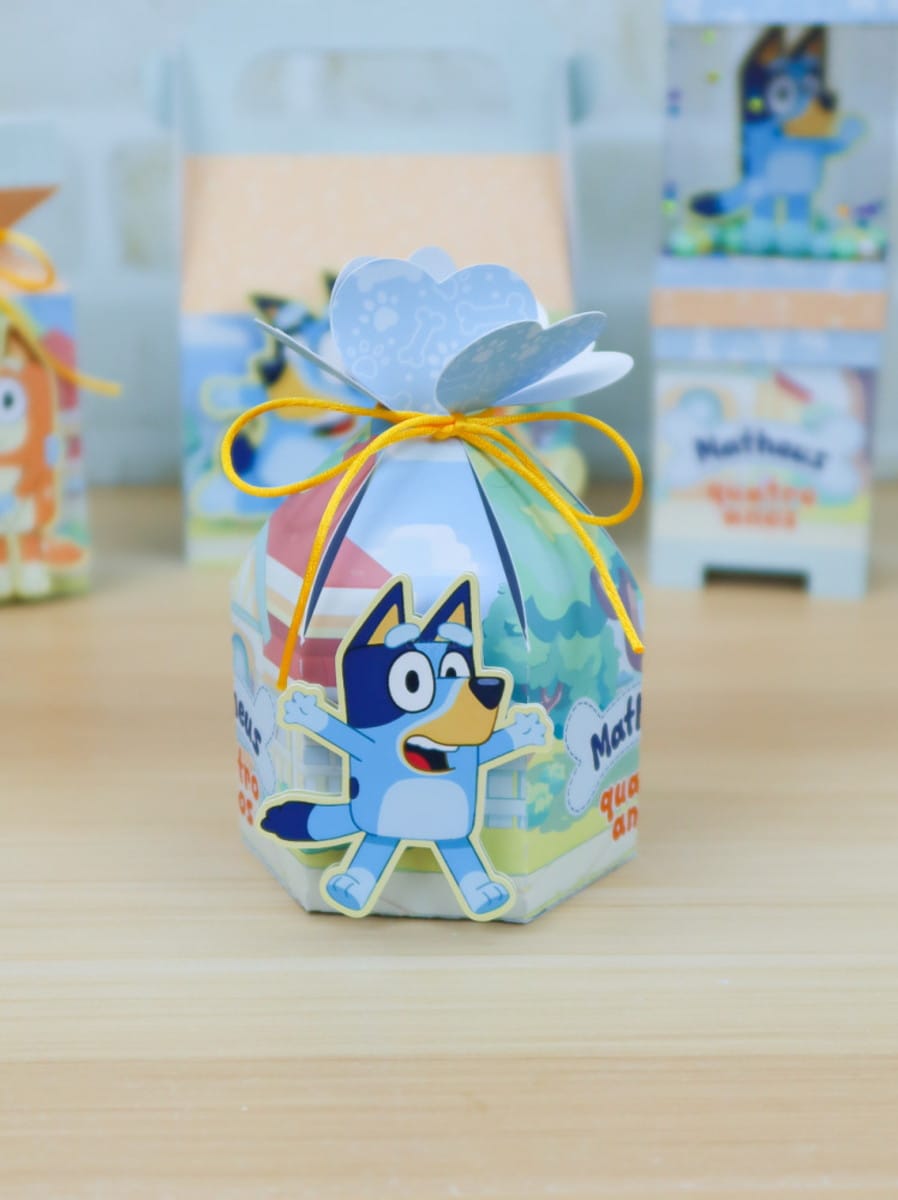 Kit Festa Bluey Arquivo Studio para Silhouette 5 Caixinha de papel decorada com personagem azul em cima de uma mesa de madeira.