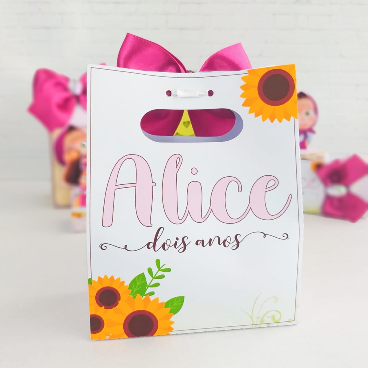 Kit Digital Completo Marsha e o Urso em PDF e Studio 5 Sacola de presente personalizada branca com laço rosa, texto e girassóis.