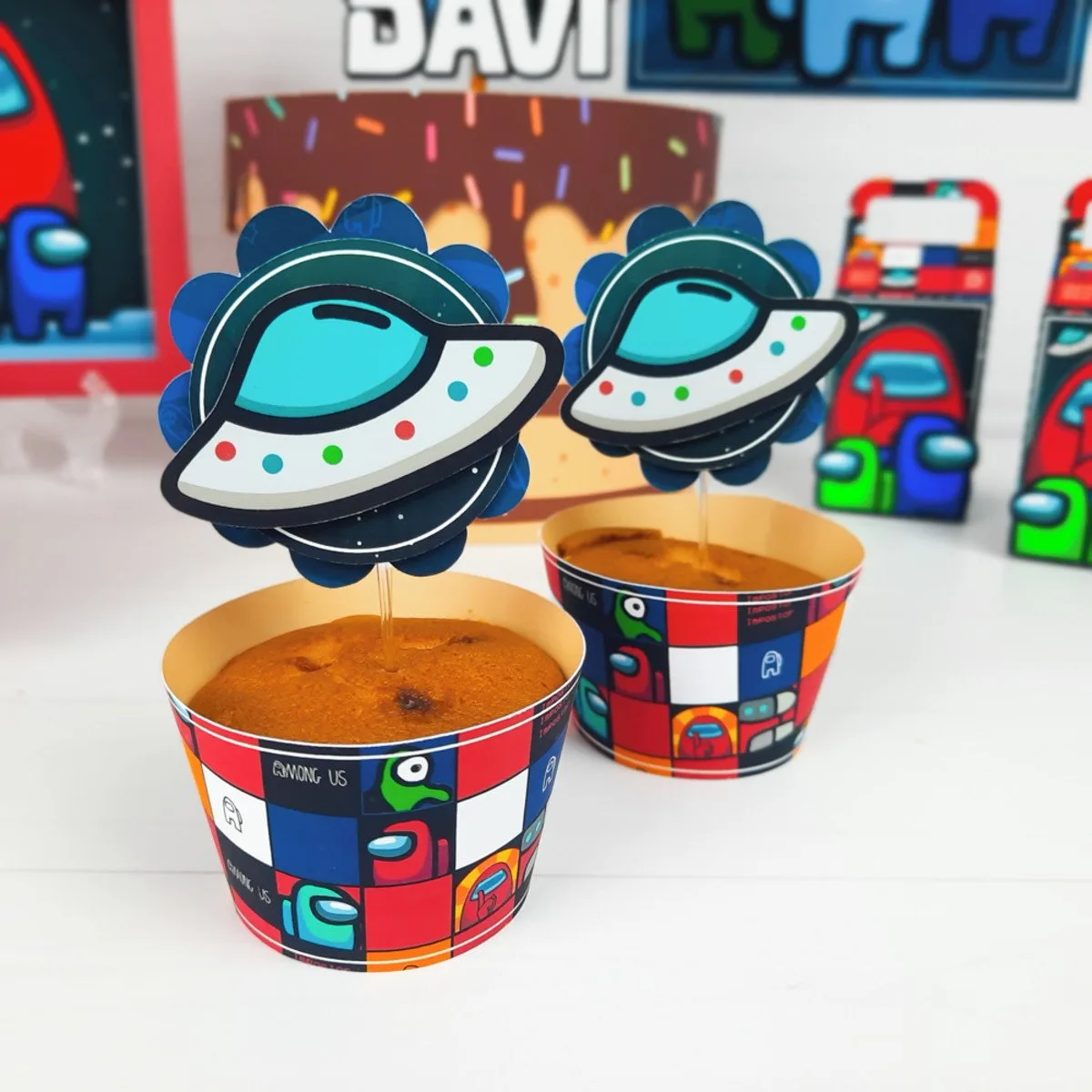 Dois cupcakes decorados com toppers de naves espaciais em copos coloridos.