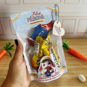 Sacola de Páscoa transparente com doces, coelho e mensagem festiva, segurada por uma mão.