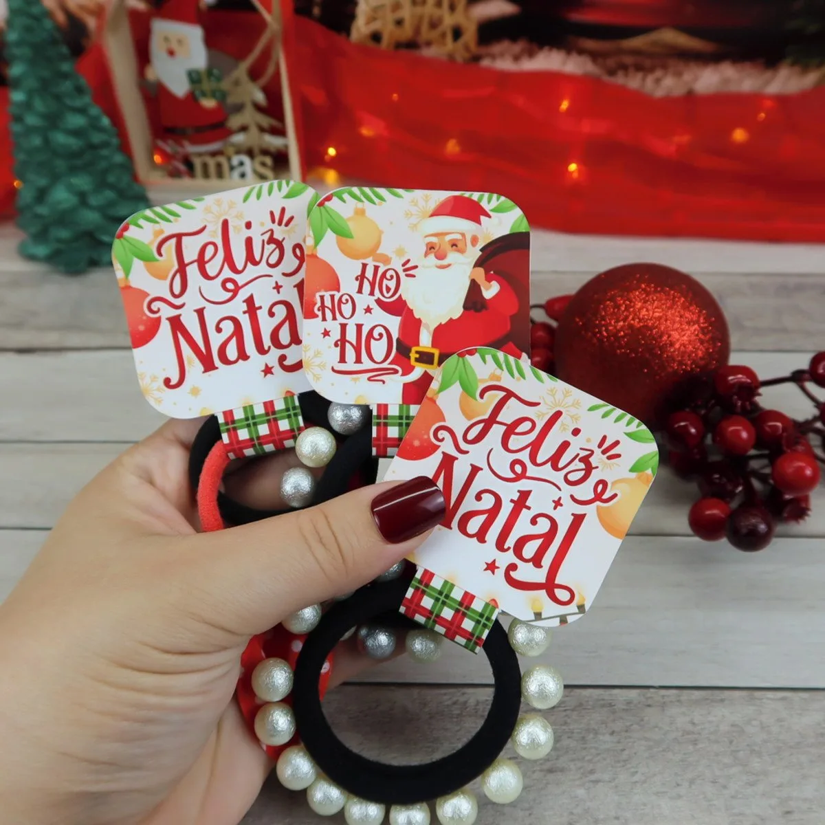 Mão segurando elásticos de cabelo pretos decorados com pérolas e tags temáticas de natal.