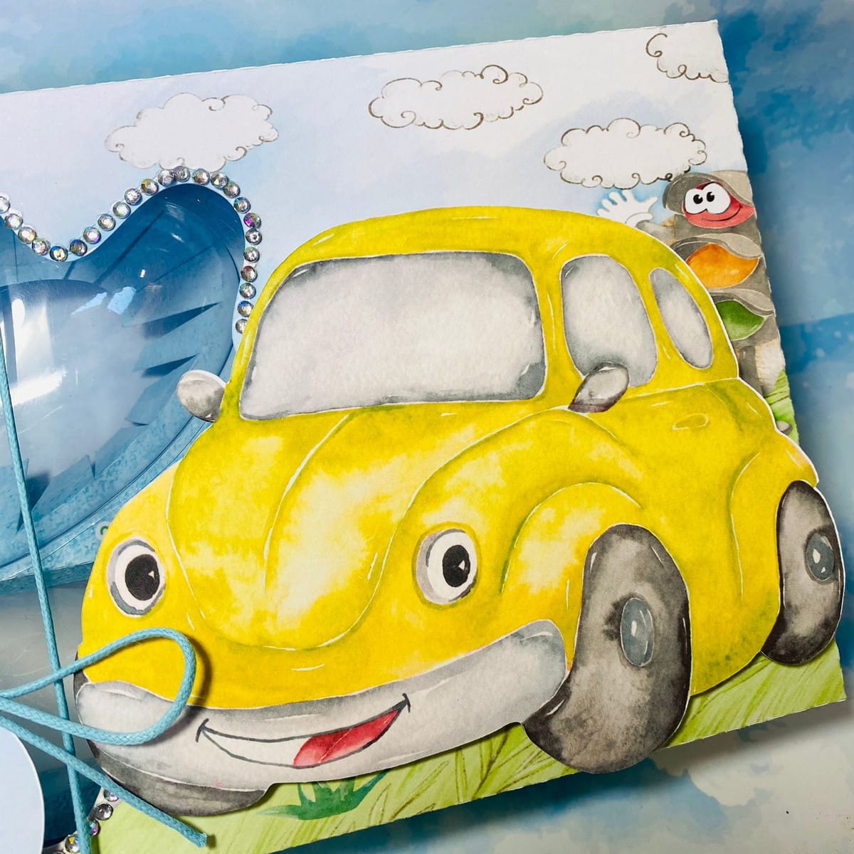 Arquivo de Corte Mini Confeiteiro Carrinho para Montar 2 Ilustração de carro amarelo sorridente, paisagem com céu, nuvens, personagem e coração azul.