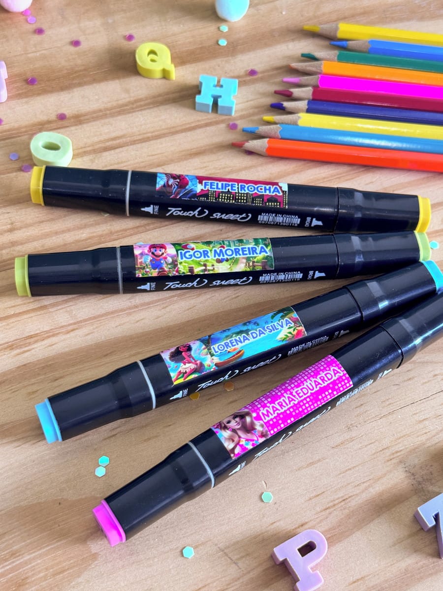 Etiquetas Escolares para Imprimir com 36 Temas Infantis 2 Quatro canetas marcadoras pretas com rótulos personalizados e coloridos em mesa de madeira.