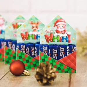 Caixinhas decoradas com temas natalinos e chocolates organizadas sobre uma mesa de madeira.