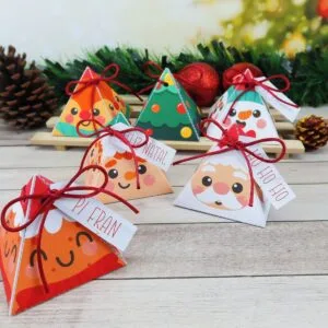 Caixinhas pirâmide de Natal decoradas com personagens e laços vermelhos sobre madeira.