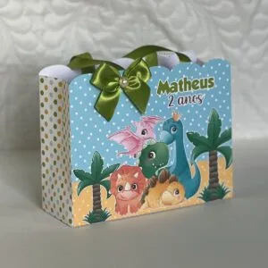 Sacola de papel com ilustrações de dinossauros e palmeiras decorada com laço verde.